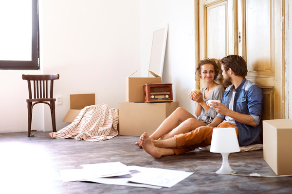 Couple sitting on floor drinking coffee surrounded by moving boxes