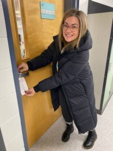 Sarah hanging 'You've Been Elfed' door hanger on the door at the school